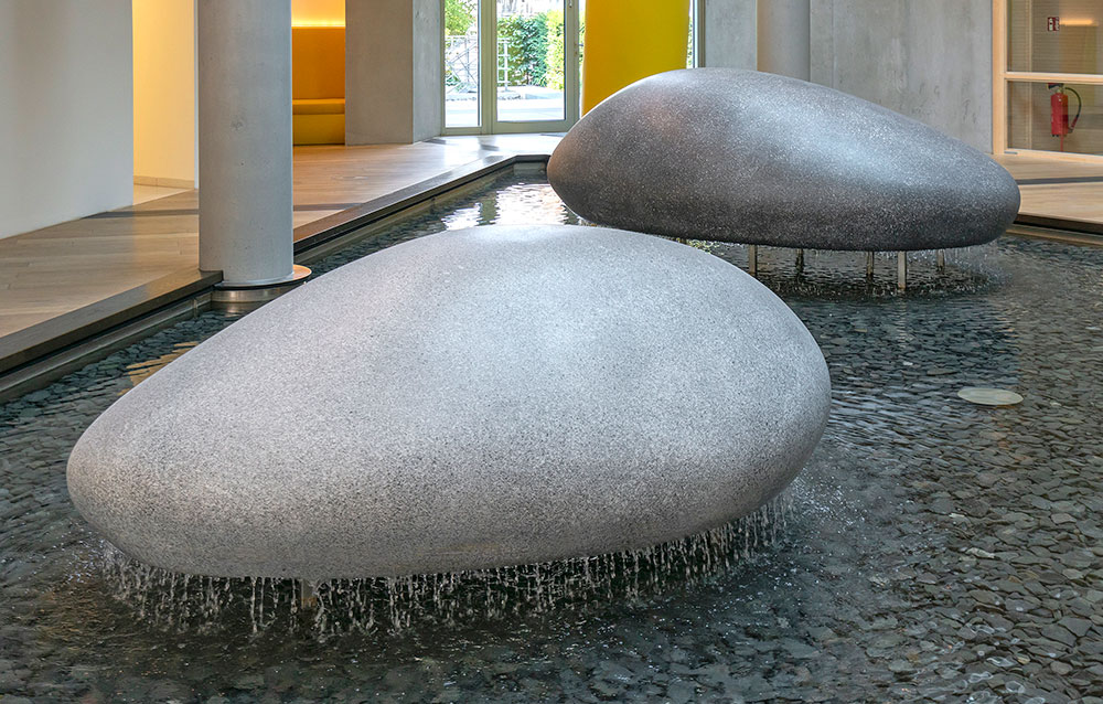 steine-glasfaserbeton-lva-muenster-detailansicht Ein umlaufender kleiner Wasserfall an den Steinen lässt die Steine über der Wasserfläche schweben